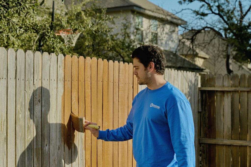 handyman applying stain to a fence with a paintbrush