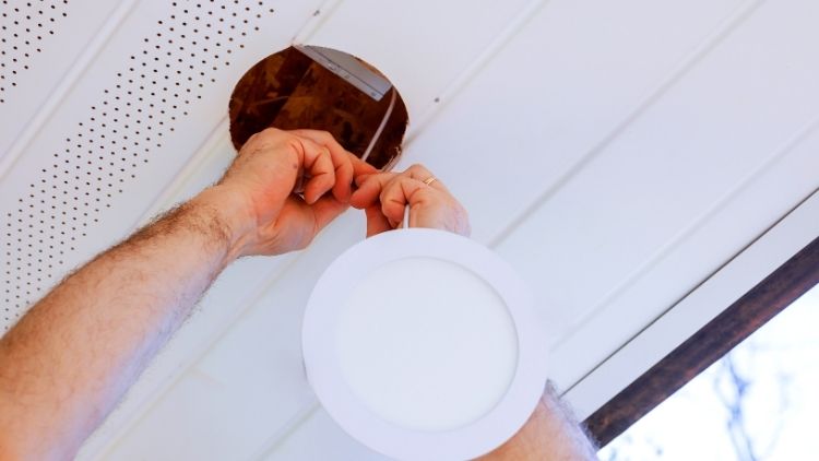 Man installs recessed lighting fixture in ceiling