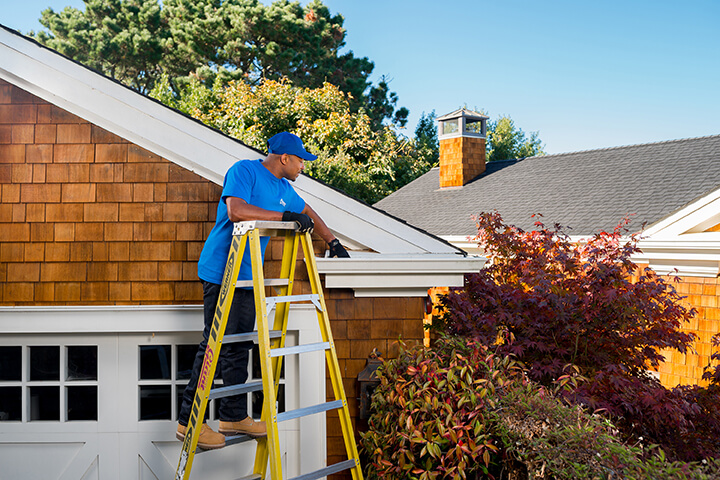 handyman standing on a ladder cleaning a home's gutter